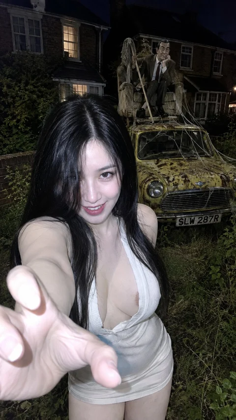 A person in a pale dress reaches toward the camera in a dark garden with greenery and stone figures.