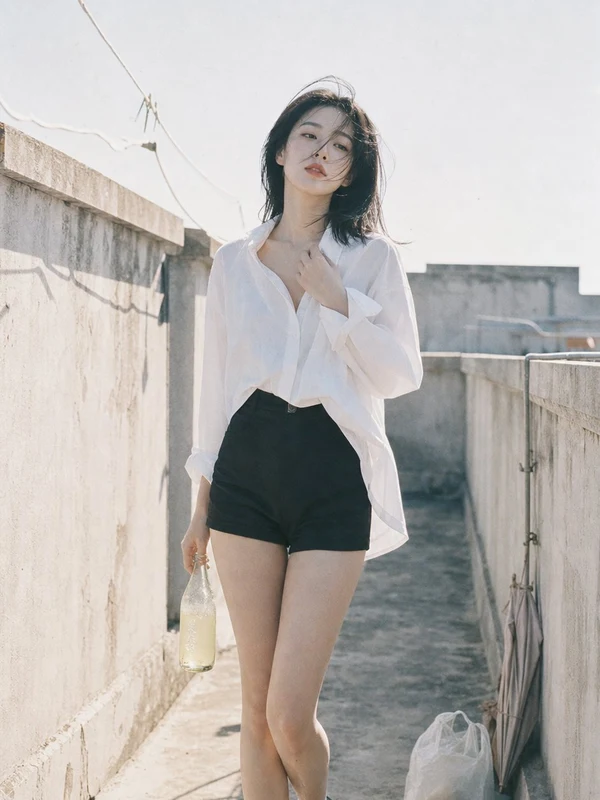 Woman in a white shirt and tailored shorts beside a sunlit wall